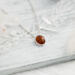  A playful 18" sterling silver necklace with a 10mm Baltic amber oval pendant on a light wood table, surrounded by soft decor. 

